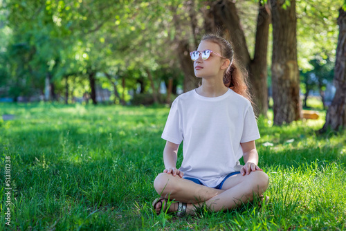 Teenage girl in white tee basic youth apparel shoot. A girl in sunglasses sits on the grass in a city park. Solid color clothing with space for text or pattern. 