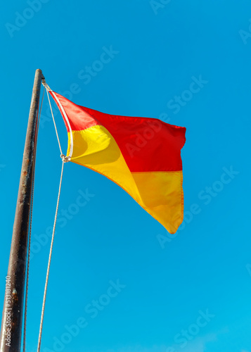 Red and yellow warning flag on the beach close up against the blue sky. Bottom view