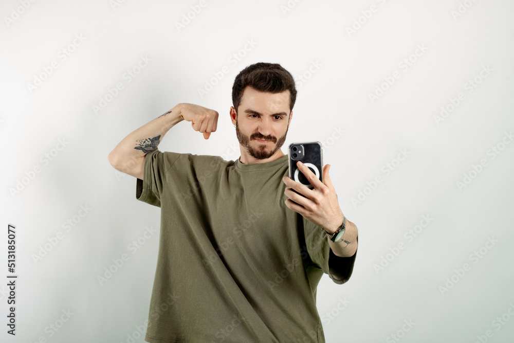 Handsome young man wearing casual clothes posing isolated over white background taking selfie, showing strong arm, flexing biceps and posing for photo. Handsome young man wearing casual clothes posing isolated over white background taking selfie, showing strong arm, flexing biceps and posing for photo.