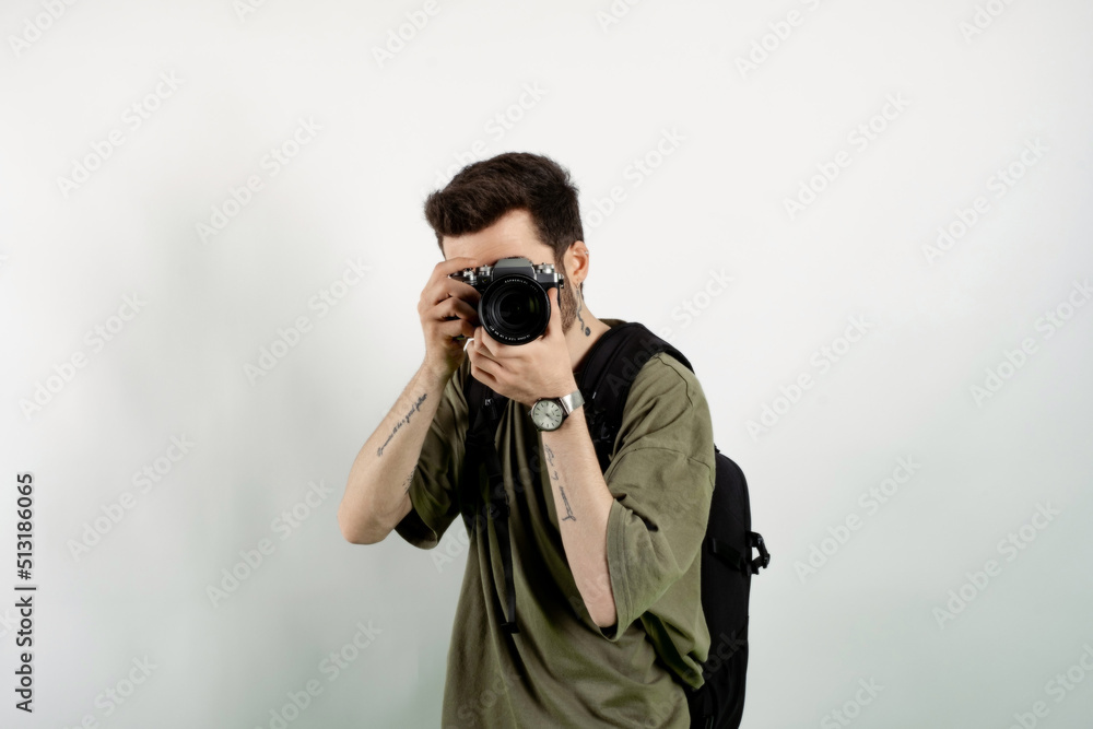 Portrait of young caucasian man wearing t-shirt posing isolated over white background taking images with dslr camera. Photographer covering his face with the camera. Portrait of young caucasian man wearing t-shirt posing isolated over white background taking images with dslr camera. Photographer covering his face with the camera.