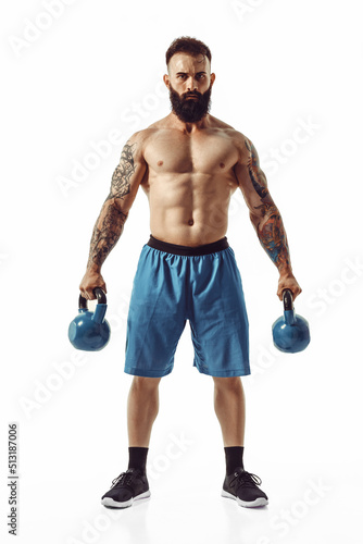 Muscular shirtless tattooed bearded male athlete bodybuilder workout with kettlebell on a white background. Isolate