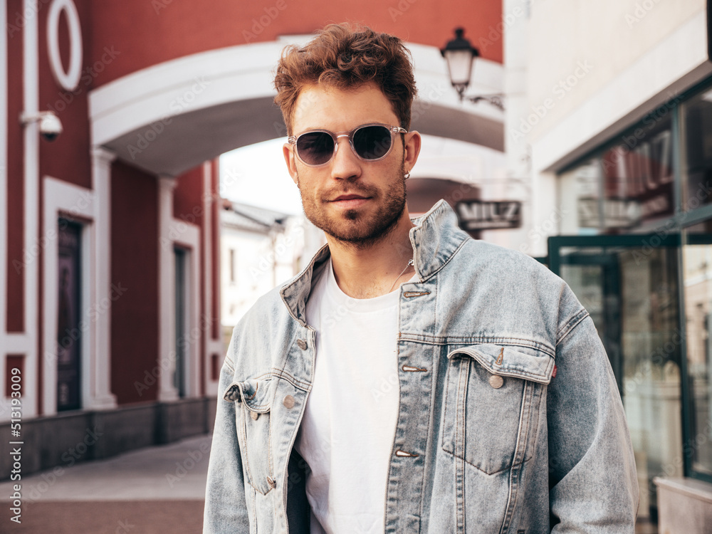Portrait of handsome confident stylish hipster lambersexual model. Sexy man dressed in jeans jacket. Fashion male posing in the street in sunglasses in Europe city. Outdoors at sunset Portrait of handsome confident stylish hipster lambersexual model. Sexy man dressed in jeans jacket. Fashion male posing in the street in sunglasses in Europe city. Outdoors at sunset