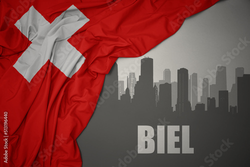 abstract silhouette of the city with text Biel near waving national flag of switzerland on a gray background.