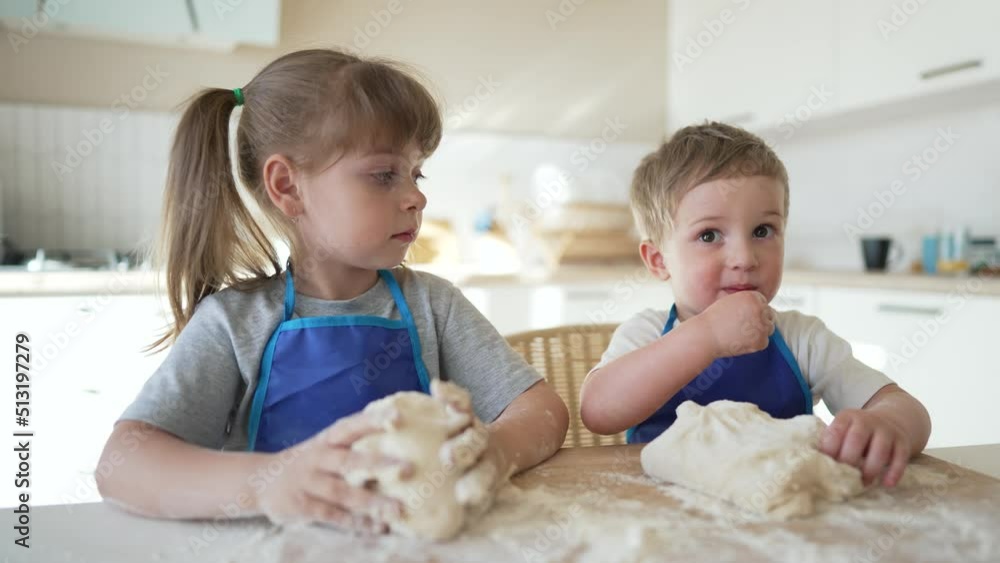 Happy family of cheerful children are preparing dough. Kids in kitchen at table share pizza. Joyful smiles of kids. Dirty children hands knead dough. Kids cooks in an apron at table bake a cake. Happy family of cheerful children are preparing dough. Kids in kitchen at table share pizza. Joyful smiles of kids. Dirty children hands knead dough. Kids cooks in an apron at table bake a cake.