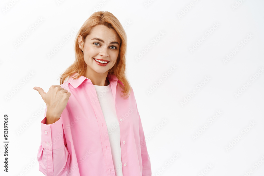 Portrait of redhead girl points finger left, shows advertisement, website logo or product banner, stands in casual clothes over white background Portrait of redhead girl points finger left, shows advertisement, website logo or product banner, stands in casual clothes over white background