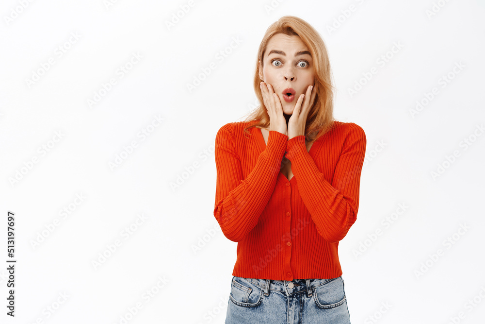Shocked young woman looking amazed, drop jaw, staring with impressed face expression at camera, stands over white background Shocked young woman looking amazed, drop jaw, staring with impressed face expression at camera, stands over white background
