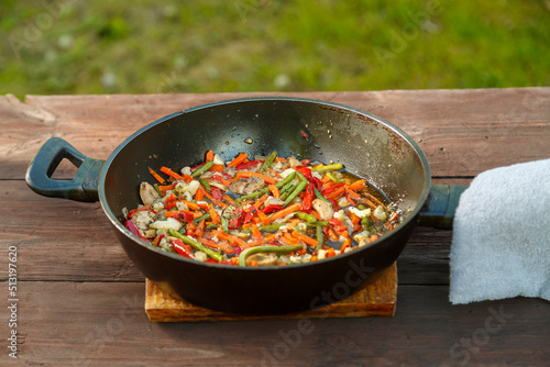 Frying pan with stewed vegetables on a stand on a wooden table. Horizontal photo