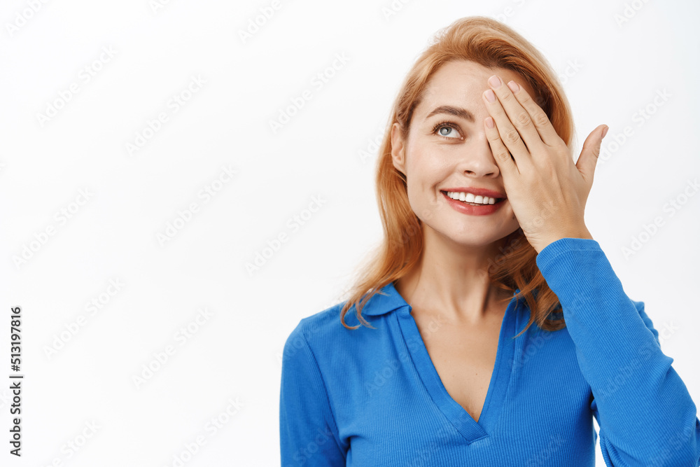Close up portrait of enthusiastic beautiful woman, 30 years old, she covers one eye and looks amazed, stands over white background Close up portrait of enthusiastic beautiful woman, 30 years old, she covers one eye and looks amazed, stands over white background