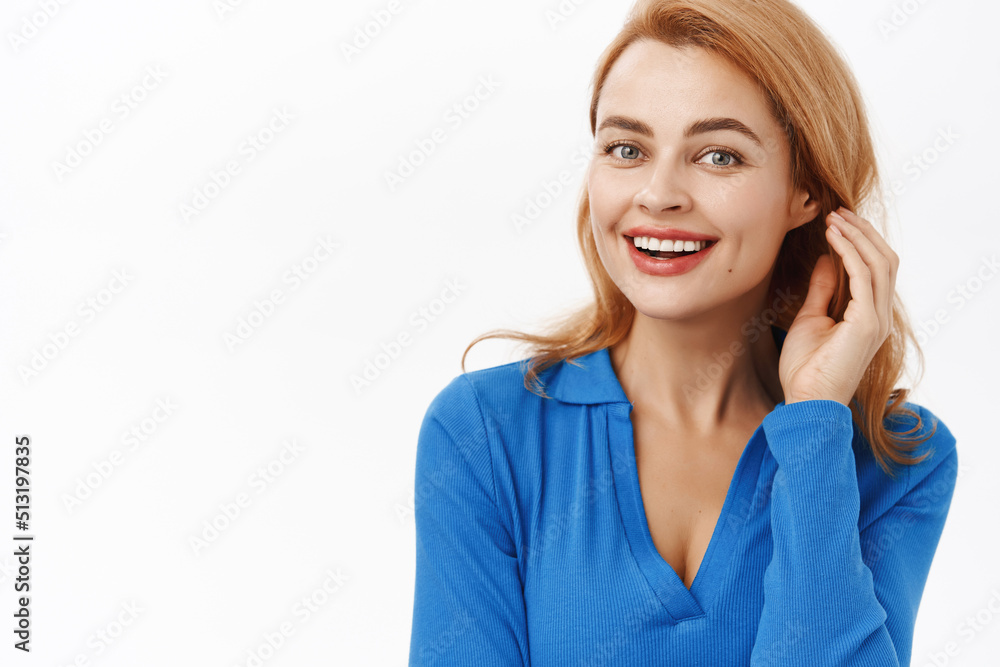 Close up of young smiling caucasia woman, tuck hair behind ear and looking happy, posing in blue blouse over white background Close up of young smiling caucasia woman, tuck hair behind ear and looking happy, posing in blue blouse over white background