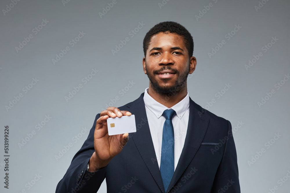 Portrait of smiling black businessman holding blank credit card mockup and showing to camera with grey background, copy space Portrait of smiling black businessman holding blank credit card mockup and showing to camera with grey background, copy space