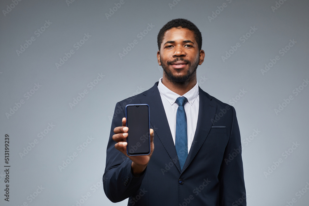 Portrait of smiling black businessman holding blank smartphone mockup and showing to camera with grey background, copy space Portrait of smiling black businessman holding blank smartphone mockup and showing to camera with grey background, copy space