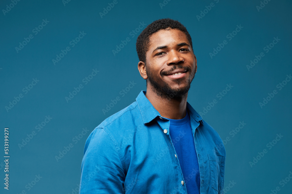 Portrait of smiling African American man wearing blue on blue background and looking at camera, copy space Portrait of smiling African American man wearing blue on blue background and looking at camera, copy space