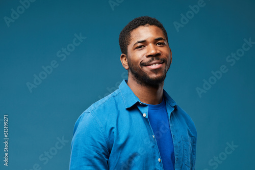 Portrait of smiling African American man wearing blue on blue background and looking at camera  copy space