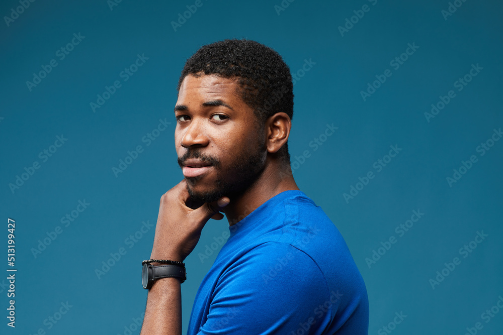 Portrait of handsome black man looking at camera over shoulder with smug expression while wearing blue on blue background, copy space Portrait of handsome black man looking at camera over shoulder with smug expression while wearing blue on blue background, copy space