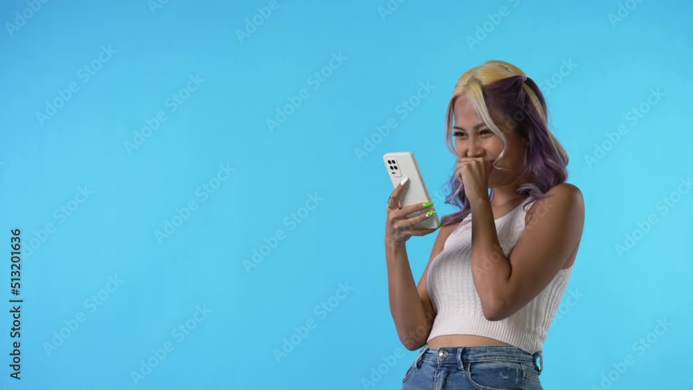 Happy and cheerful young Asian woman using smartphone isolated on blue background Happy and cheerful young Asian woman using smartphone isolated on blue background