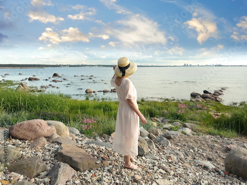  women in pink dress and straw hat wild beach with flowers and green bush on horizon relax on blue sea and cloudy sky nature landscape 