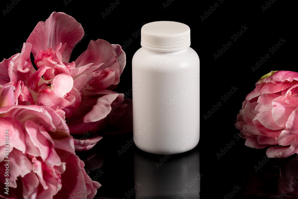 White bottle with pills. Jar of medicine. The photo was taken on a black background with flowers on both sides White bottle with pills. Jar of medicine. The photo was taken on a black background with flowers on both sides