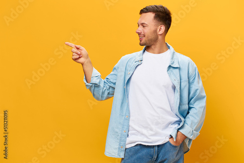 Happy cheerful tanned handsome man in blue basic t-shirt point finger look aside posing isolated on orange yellow studio background. Copy space Banner Mockup. People emotions Lifestyle concept