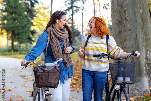 Two woman push bikes and talk funny stories and smile in public park