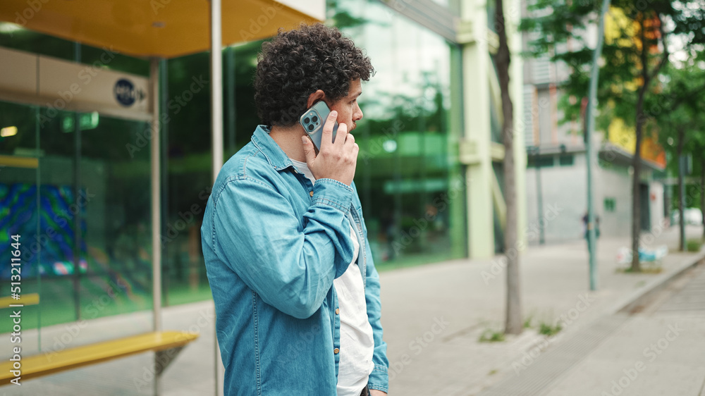 young bearded man in denim shirt stands at bus stop waiting for bus and talking on mobile phone on modern city background young bearded man in denim shirt stands at bus stop waiting for bus and talking on mobile phone on modern city background