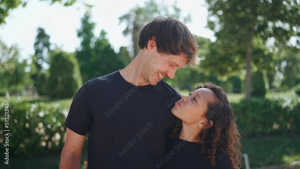 Cheerful father hugging his multiethnic daughter and looking at the camera in the park at summer Cheerful father hugging his multiethnic daughter and looking at the camera in the park at summer