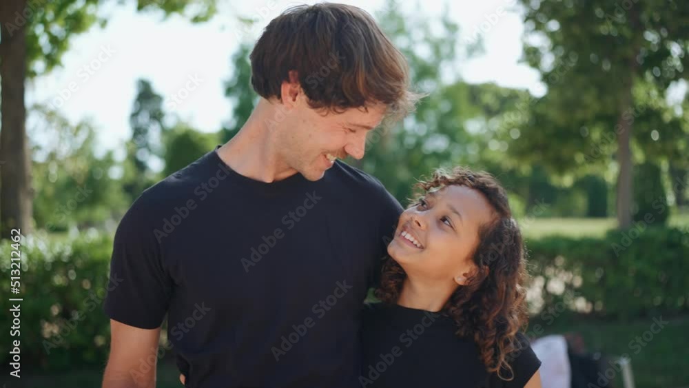 Smiling father hugging his multiethnic daughter and looking at her in the park at summer Smiling father hugging his multiethnic daughter and looking at her in the park at summer