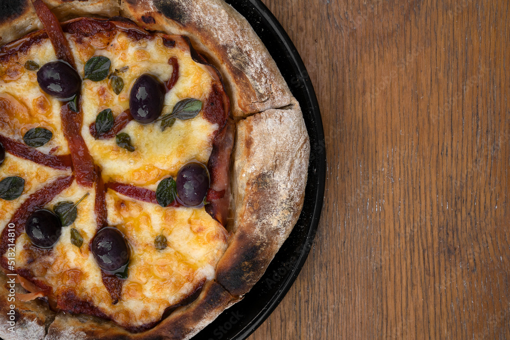 Pizza. Top view of a pizza with mozzarella cheese, grilled red bell peppers, ham, black olives and fresh oregano leaves, on the wooden table. Pizza. Top view of a pizza with mozzarella cheese, grilled red bell peppers, ham, black olives and fresh oregano leaves, on the wooden table.