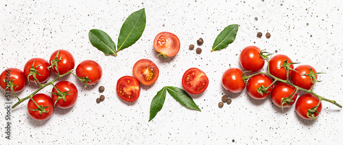 Ripe juicy cherry tomatoes with bay leaves and allspice on white marble background top view. 