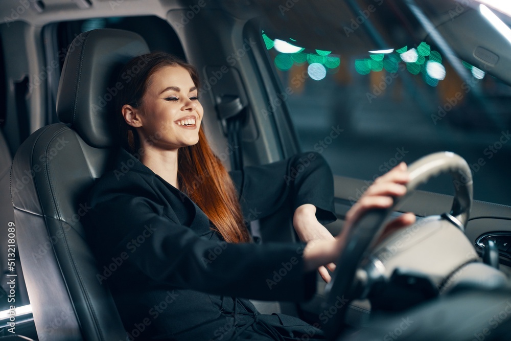 a happy, relaxed woman enjoys a night ride at the wheel while sitting in a car and smiling broadly squints her eyes with happiness