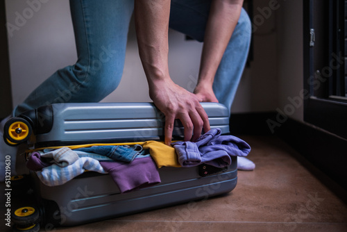 a person trying to fit a lot of things in a suitcase, preparation for a one-person holiday at home