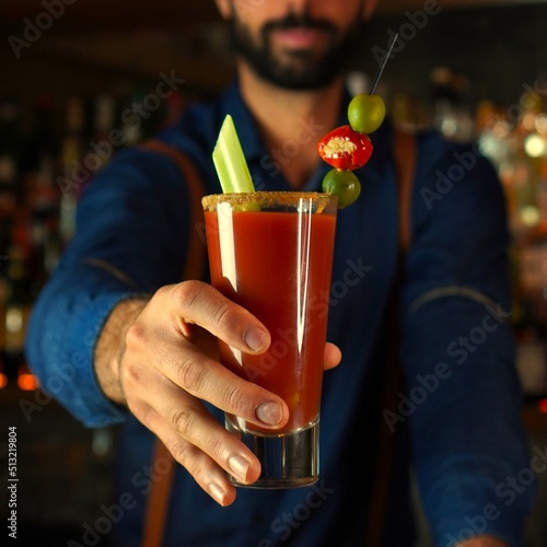 Bartender prepares a red signature cocktail and offers it to his clients, bloody Mary cocktail, concept enjoy the night
