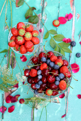 Glass bowls with fresh summer berries on old wooden table. Breakfast in the garden. Blueberry, strawberry, sweet cherry close up photo. 