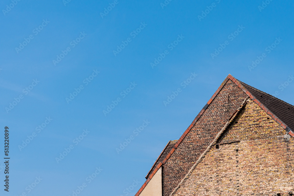 Fragment of an old tiled roof against the blue sky. The building is made of red brick. Fragment of an old tiled roof against the blue sky. The building is made of red brick.