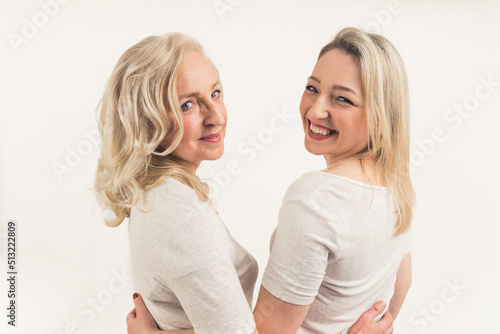 Back shot of two attractive affectionate blonde middle-aged women holding each other passionately, turning towards camera. High quality photo