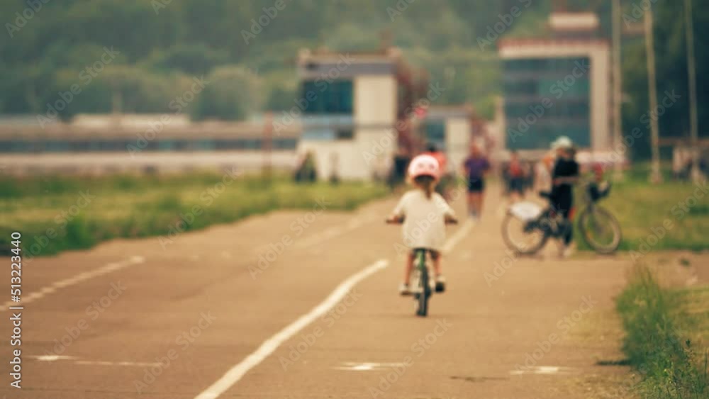 Unknown blurred kid cycling along the park pathway, slow motion Unknown blurred kid cycling along the park pathway, slow motion