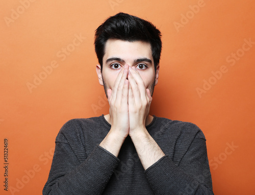 A young handsome man covers his mouth with his palms