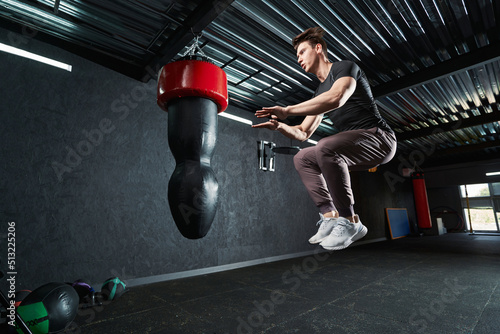 Sportsman doing tuck jumps in front of hanging punching bag © Viacheslav Yakobchuk