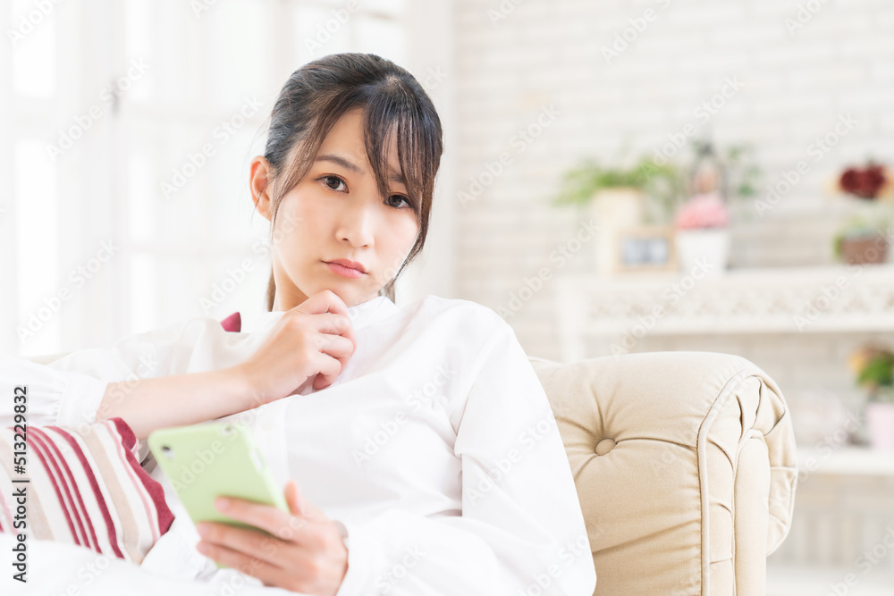 部屋でスマホを見る女性　考える