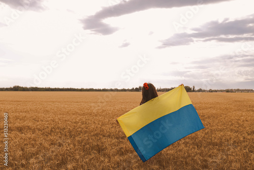 Young pretty girl holds flag and waiting for victory in the field wearing Ukrainian national embroidered shirt with red wreath. Concept of Ukraine Independence  freedom and stop the war. Peace in word