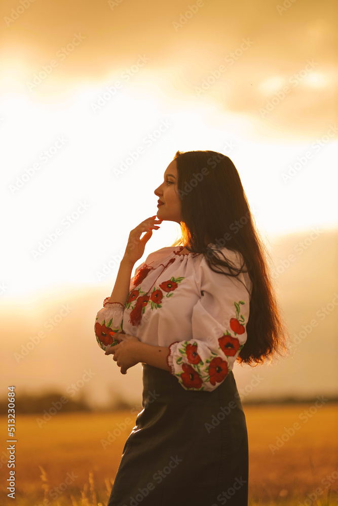 Young girl is standing in the wheat field wearing Ukrainian national ethnic  embroidered shirt at sunset yellow light. Concept of Independence of Ukraine and stop the war. Dreaming about peace in word