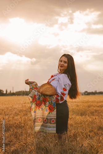 Wallpaper Mural Young girl is standing in the wheat field wearing Ukrainian national ethnic embroidered shirt and holds baked bread on national towel at sunset yellow light. Independence Day. Stop war in Ukraine Torontodigital.ca