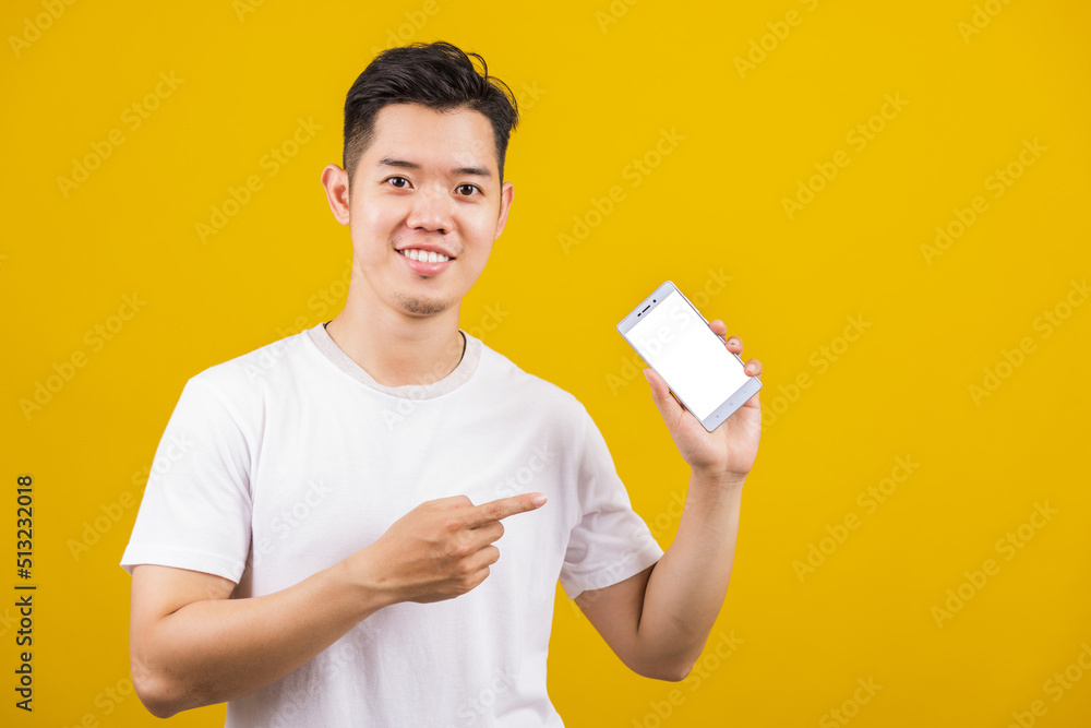 Happy Asian handsome young man smiling positive showing smartphone blank screen and pointing finger to screen, studio shot isolated on yellow background, making successful expression gesture concept Happy Asian handsome young man smiling positive showing smartphone blank screen and pointing finger to screen, studio shot isolated on yellow background, making successful expression gesture concept