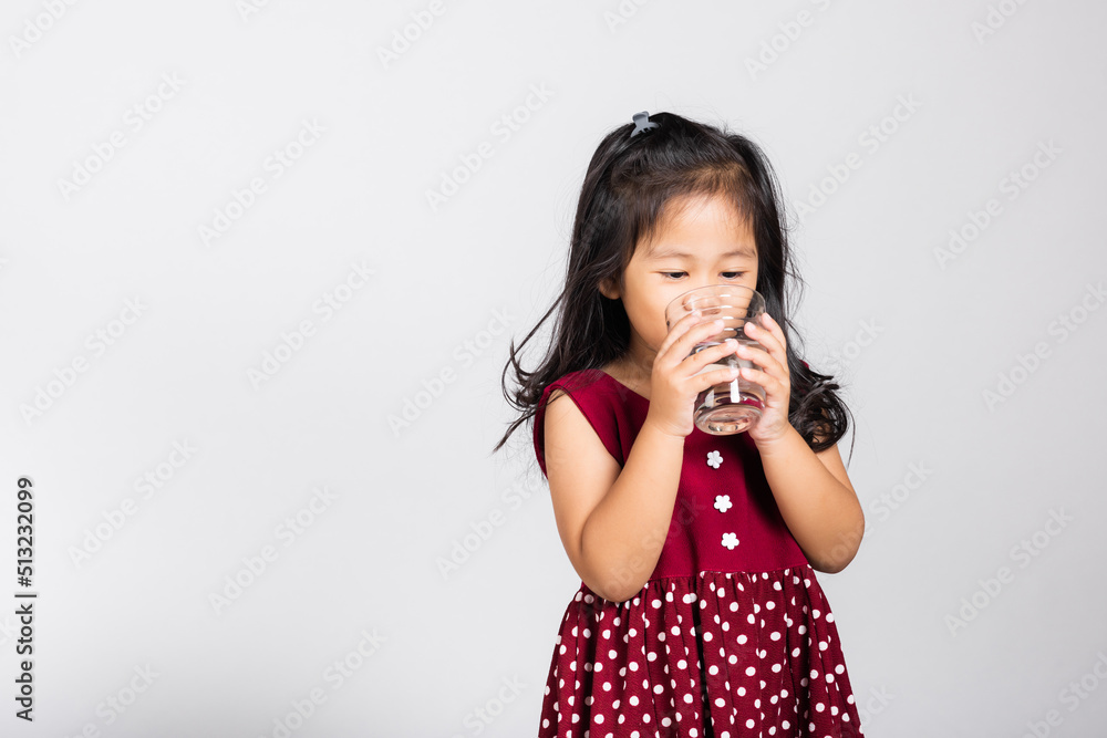 Little cute kid girl 3-4 years old smile drinking fresh water from glass in studio shot isolated on white background, Asian children preschool, Daily life health Little cute kid girl 3-4 years old smile drinking fresh water from glass in studio shot isolated on white background, Asian children preschool, Daily life health