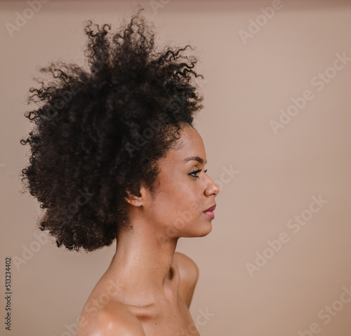 Side a smiling young Latin afro woman. Joy, positive and love. Beautiful african-style hair. Pastel studio background.