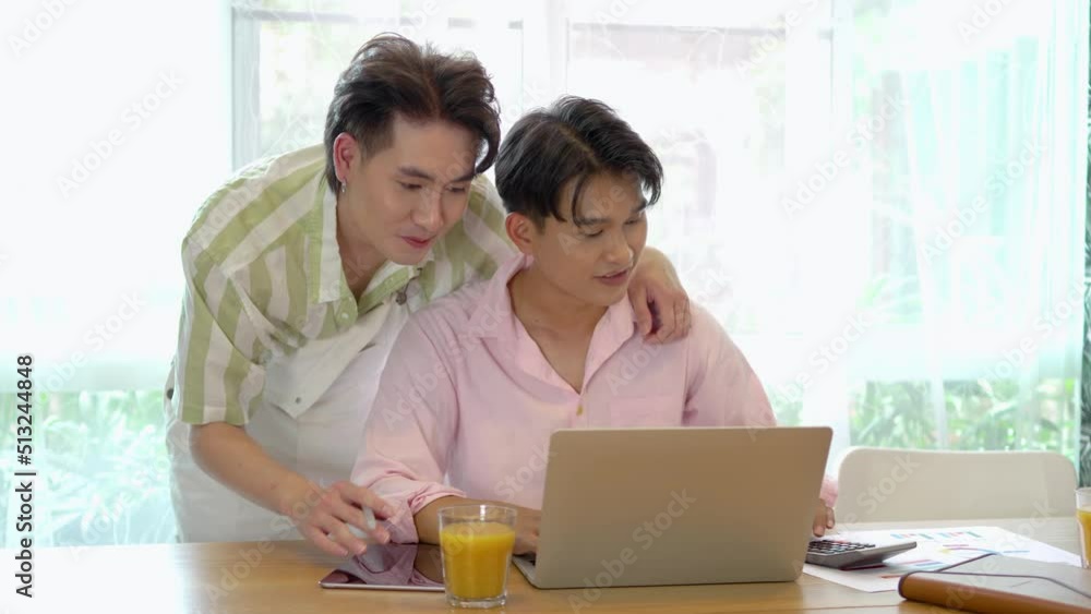 Young asian gay couple hugging and takes care of his boyfriend, surfing on internet during break, use laptop, discuss project, smiling large, give each other hi five, completed the work perfectly Young asian gay couple hugging and takes care of his boyfriend, surfing on internet during break, use laptop, discuss project, smiling large, give each other hi five, completed the work perfectly