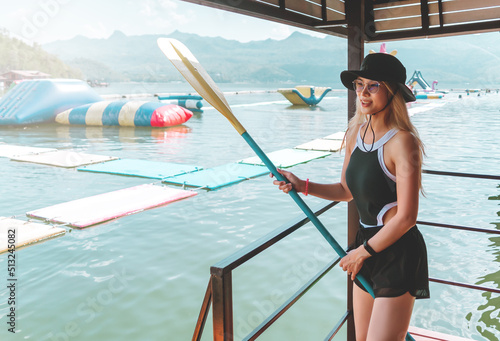 Woman in swim suit is holding a sup board paddle reading to go paddle board in a lake.