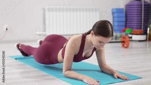 a beautiful and slender woman in a burgundy tracksuit exercises on a mat