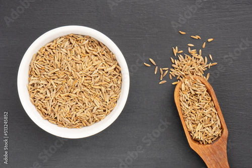 Spice cumin (jeera) in white ceramic bowl and scoop on black wooden background. Vegetarian food concept