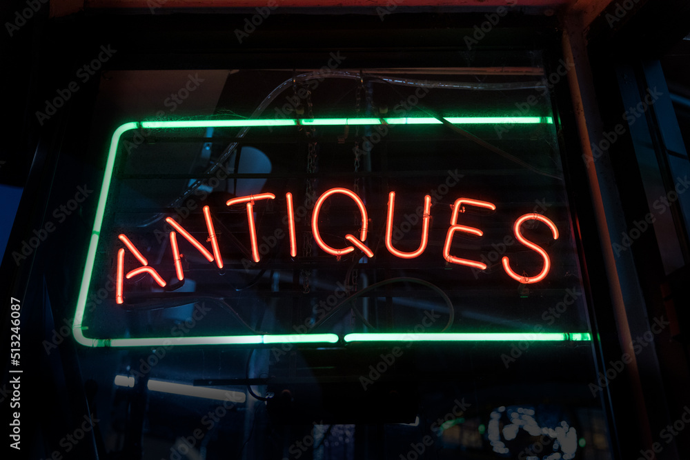 Red and green antiques sign glowing from a dark window