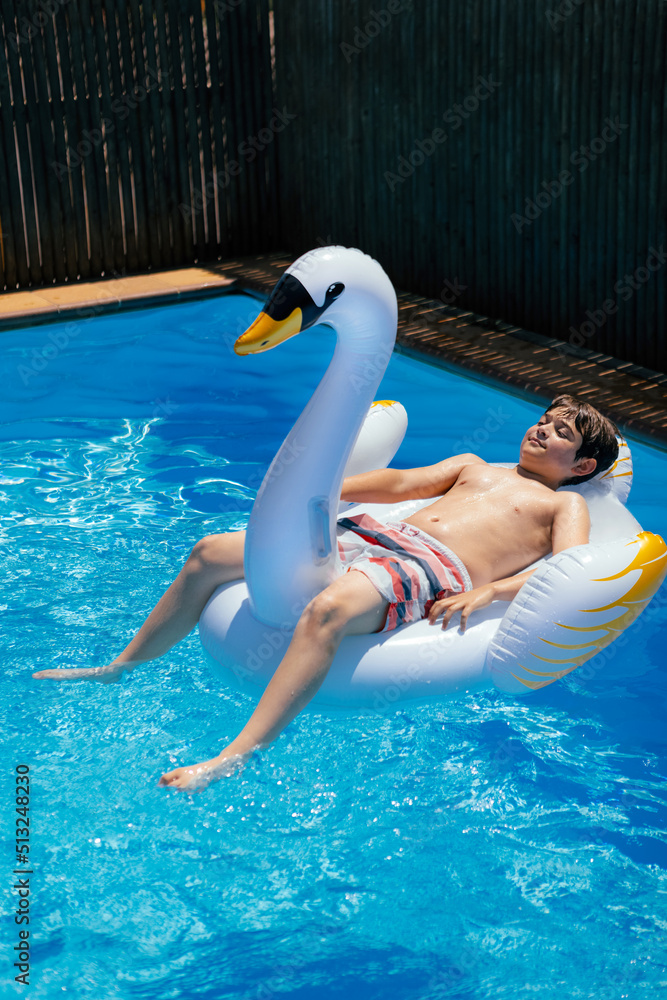 Teen boy sunbathing on inflatable swan mattress